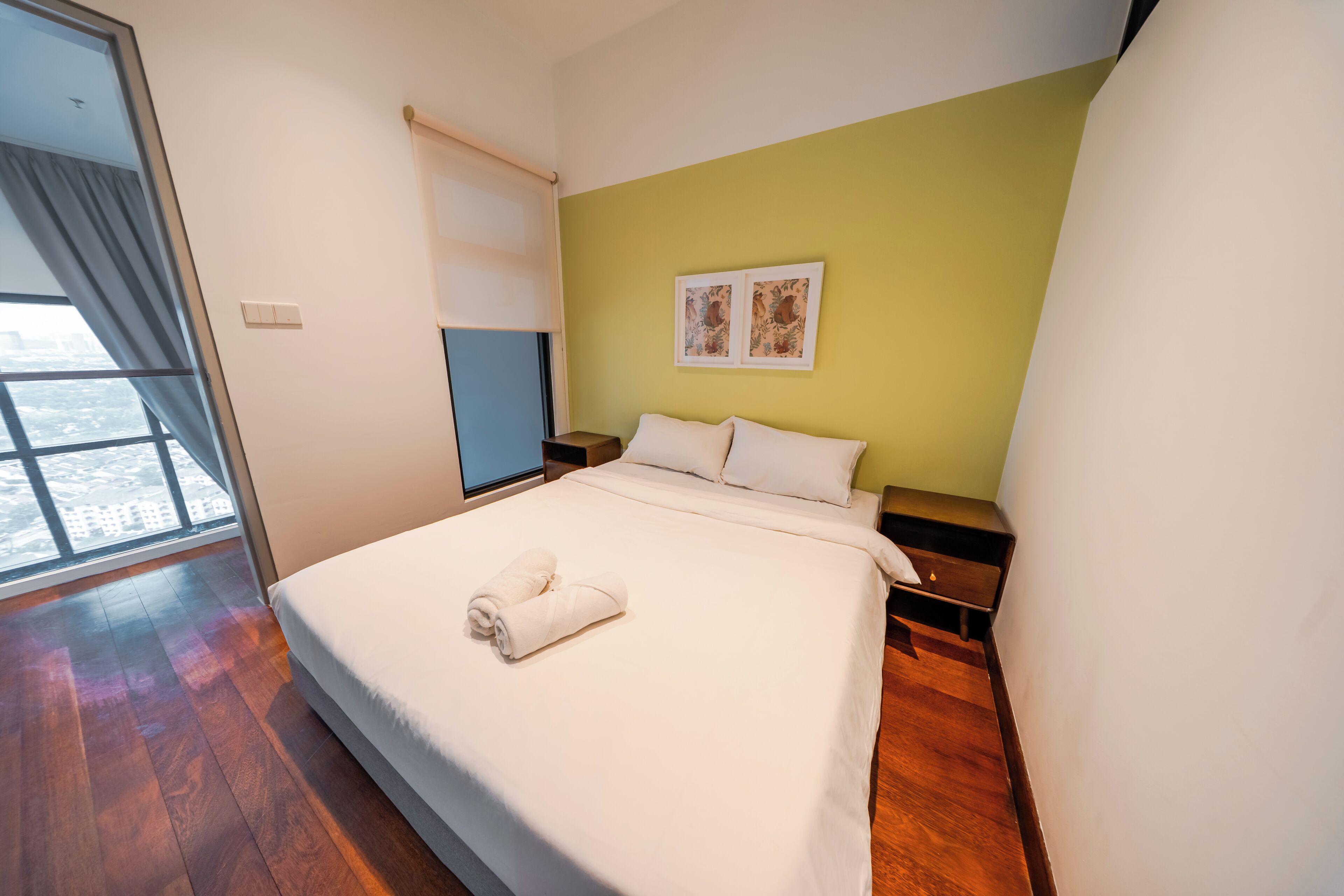 Una camera d'albergo con un letto grande, un comodino, una finestra con tende e una parete verde.