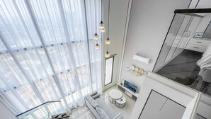 A modern kitchen with a large window, a dining area with a sofa and two round tables, and a small TV on a cabinet. - HighparkSuites Petaling Jaya Kelana Jaya (Petaling Jaya)