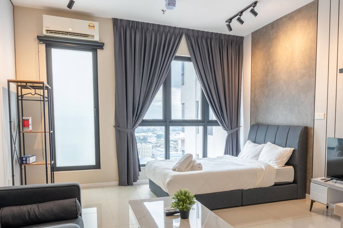 A modern hotel room with a large bed, a flat-screen TV, a desk, and a window with curtains.