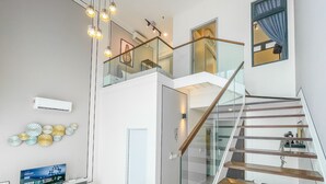 A modern interior with a glass staircase, a mounted air conditioner, and a flat-screen TV on a stand. - HighparkSuites Petaling Jaya Kelana Jaya (Petaling Jaya)