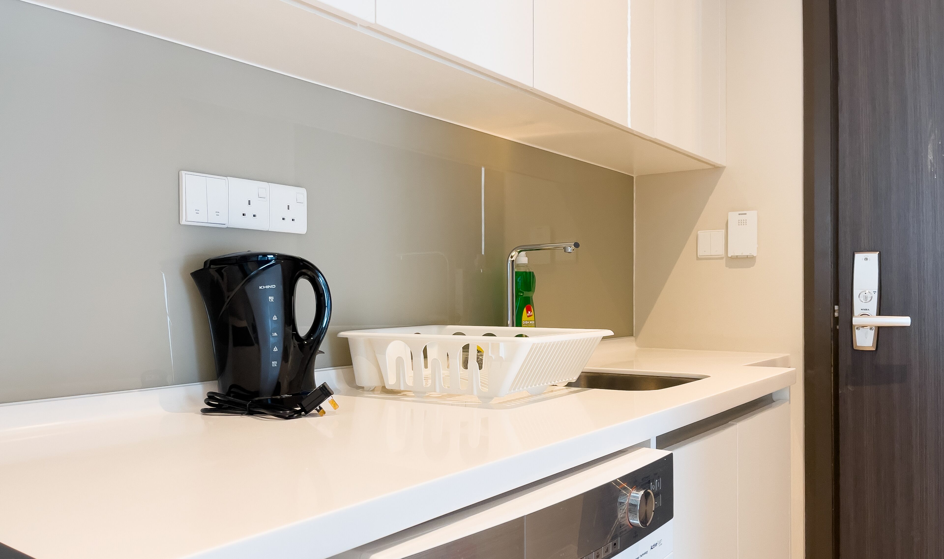 A modern kitchen with a kettle, a dish soap dispenser, and a power outlet.