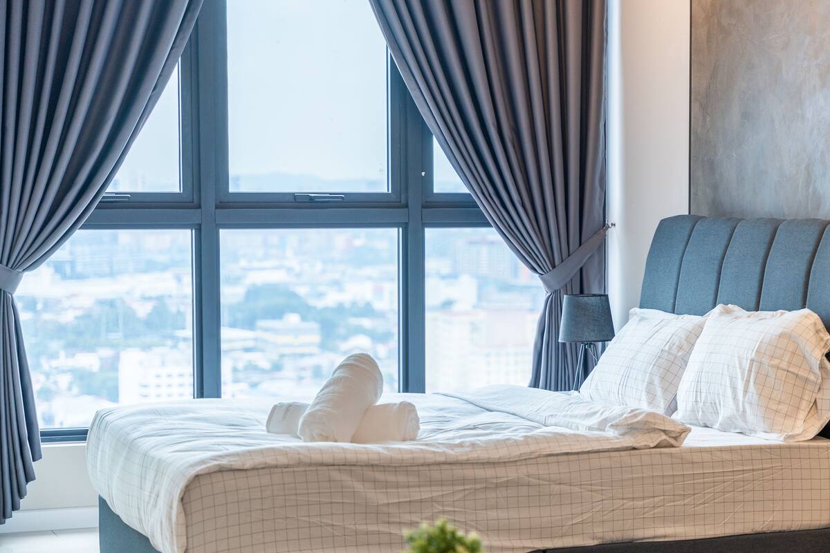 A hotel room with a large window, a bed with white bedding, and a view of a cityscape.