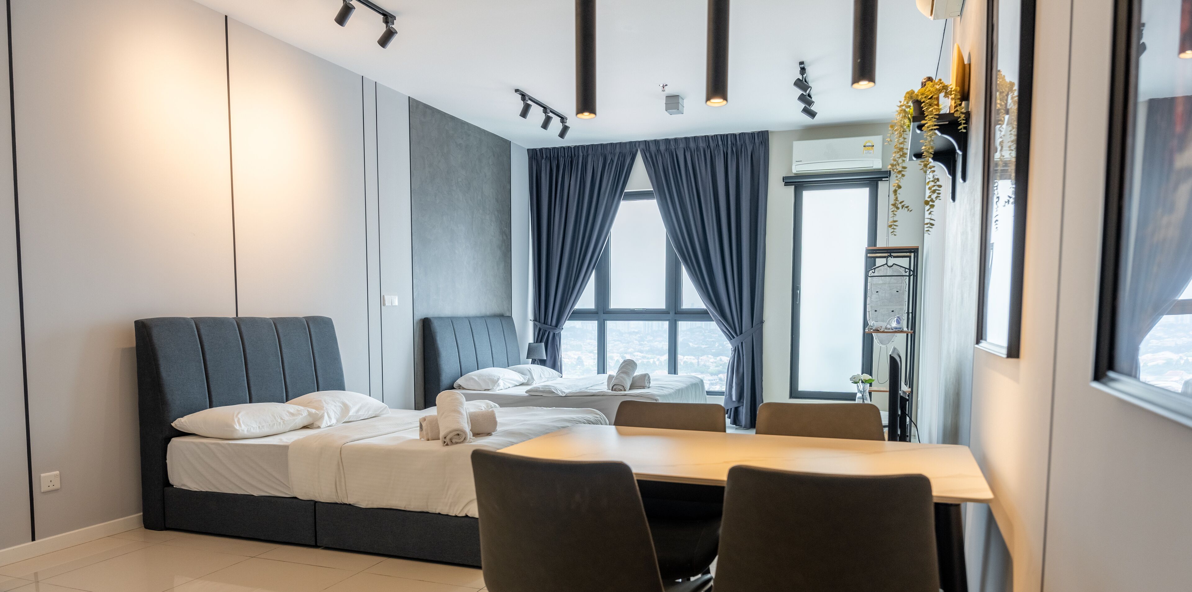 A modern hotel room with a large bed, a dining table, and a view of the city.