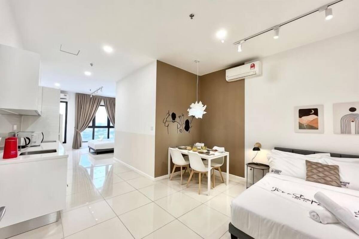 A modern hotel room with a bed, bedside table, and a dining area with chairs.