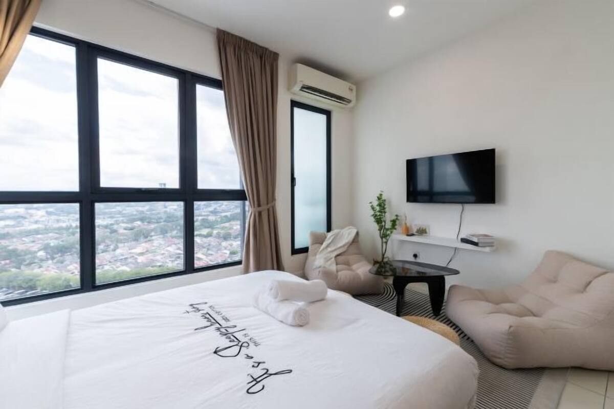 A hotel room with a large bed, a TV, a chair, and a view of the city.