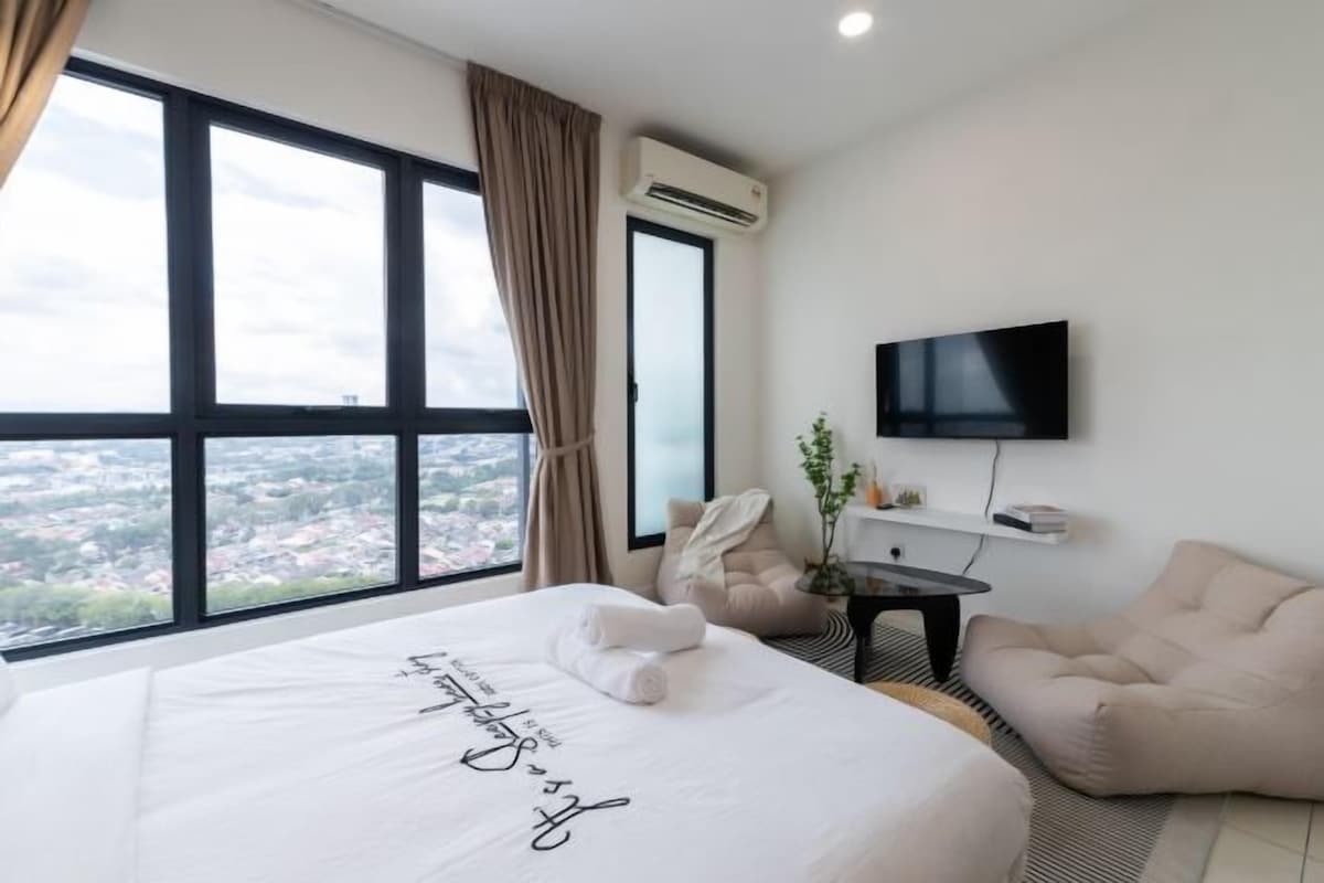 Ein Hotelzimmer mit einem großen Bett, einem Fernseher, einem Sessel und Blick auf die Stadt.