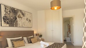 Un dormitorio ordenado con una cama grande, una mesita de noche, una lámpara y un cuadro en la pared.