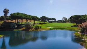 Un campo de golf con un estanque, árboles y cielo despejado.