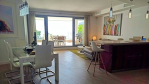 Una sala de estar moderna con una mesa de comedor de vidrio, sillas blancas, un sofá y una zona de cocina con barra.