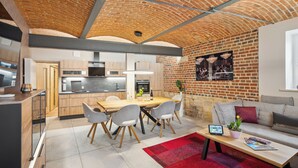 A modern kitchen with wooden cabinets, a dining table, and grey chairs. There is a red rug on the floor and a sofa with cushions in the living area. - Apartmentferienhaus Schlag (Naumburg)