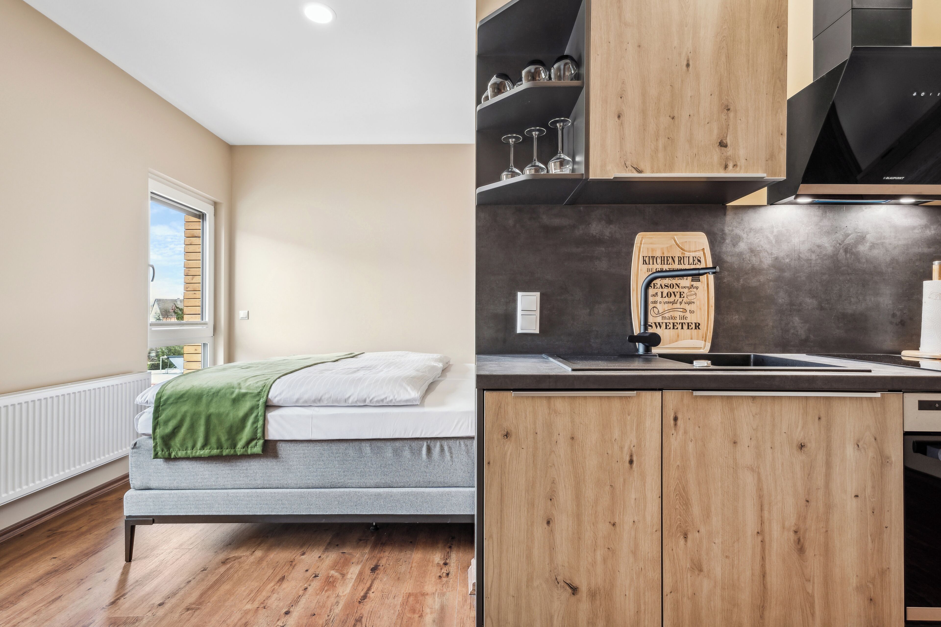 A bedroom with a bed, a window, and a view of the outside. The room has wooden flooring and a white radiator.