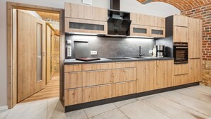 A modern kitchen with wooden cabinets, a stainless steel countertop, and a brick wall. - Apartmentferienhaus Schlag (Naumburg)