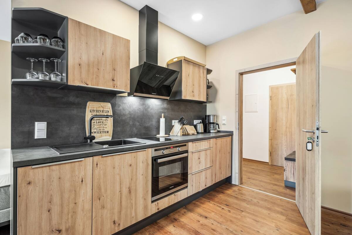 Una cocina moderna con armarios de madera, una campana extractora negra y un horno empotrado.