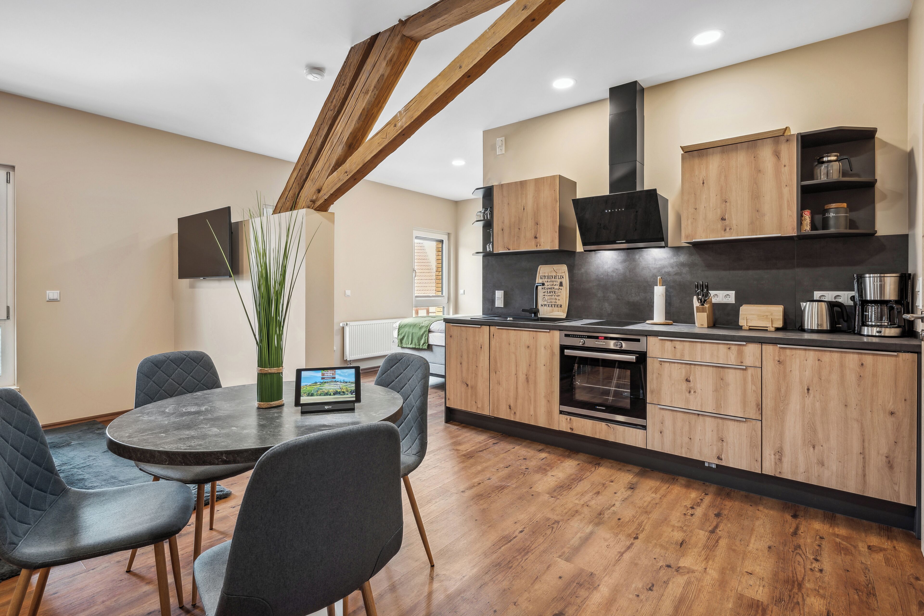 A modern kitchen with wooden cabinets, a built-in oven, and a dining area with a round table and chairs.