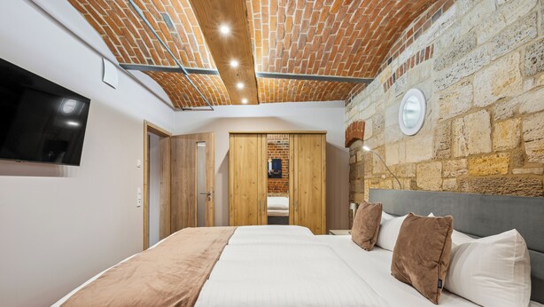 A bedroom with a brick ceiling, a large bed with white and brown bedding, a flat-screen TV mounted on the wall, and wooden wardrobes. - Apartmentferienhaus Schlag (Naumburg)