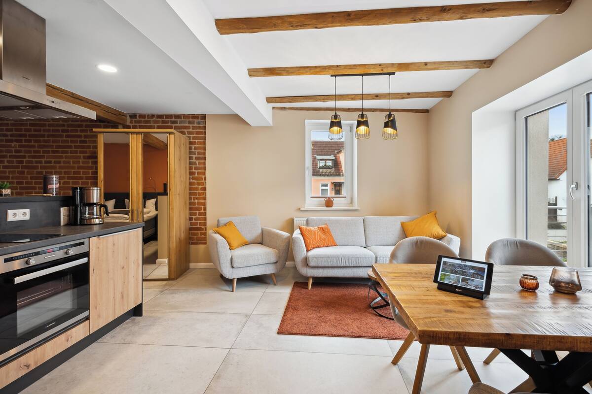 Una cocina moderna con horno integrado, un comedor con mesa y sillas de madera, y una zona de estar con sofá y sillones.