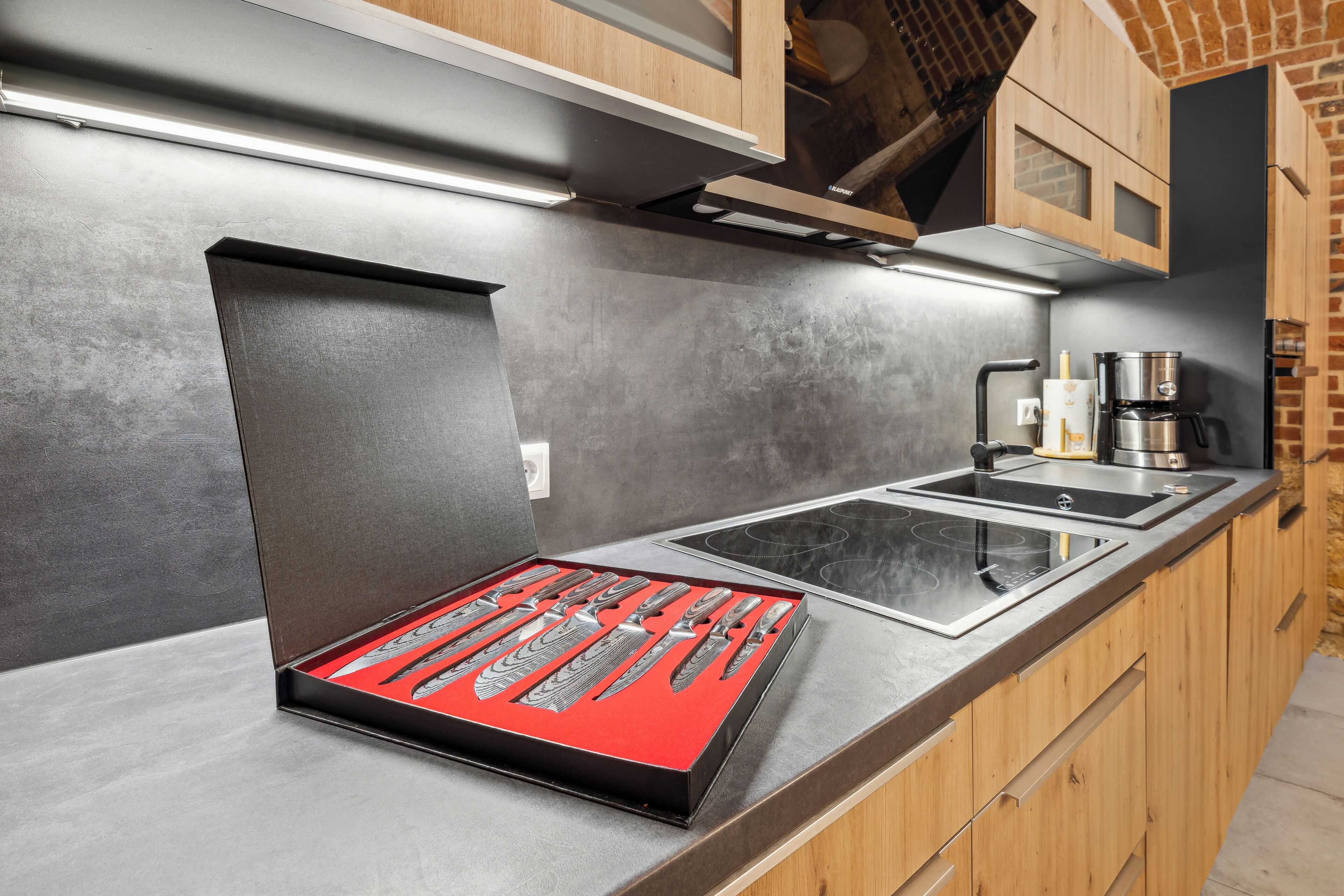 A modern kitchen with a built-in stove, wooden cabinets, and a red knife block on the countertop.