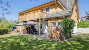 A two-story wooden house with a balcony, outdoor seating, and a covered patio area. - Moderne Ferienwohnung mit Gartenblick in Koserow (Koserow)