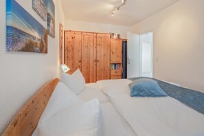 A bedroom with two beds, wooden wardrobe, and a door leading to another room. - Moderne Ferienwohnung mit Gartenblick in Koserow (Koserow)