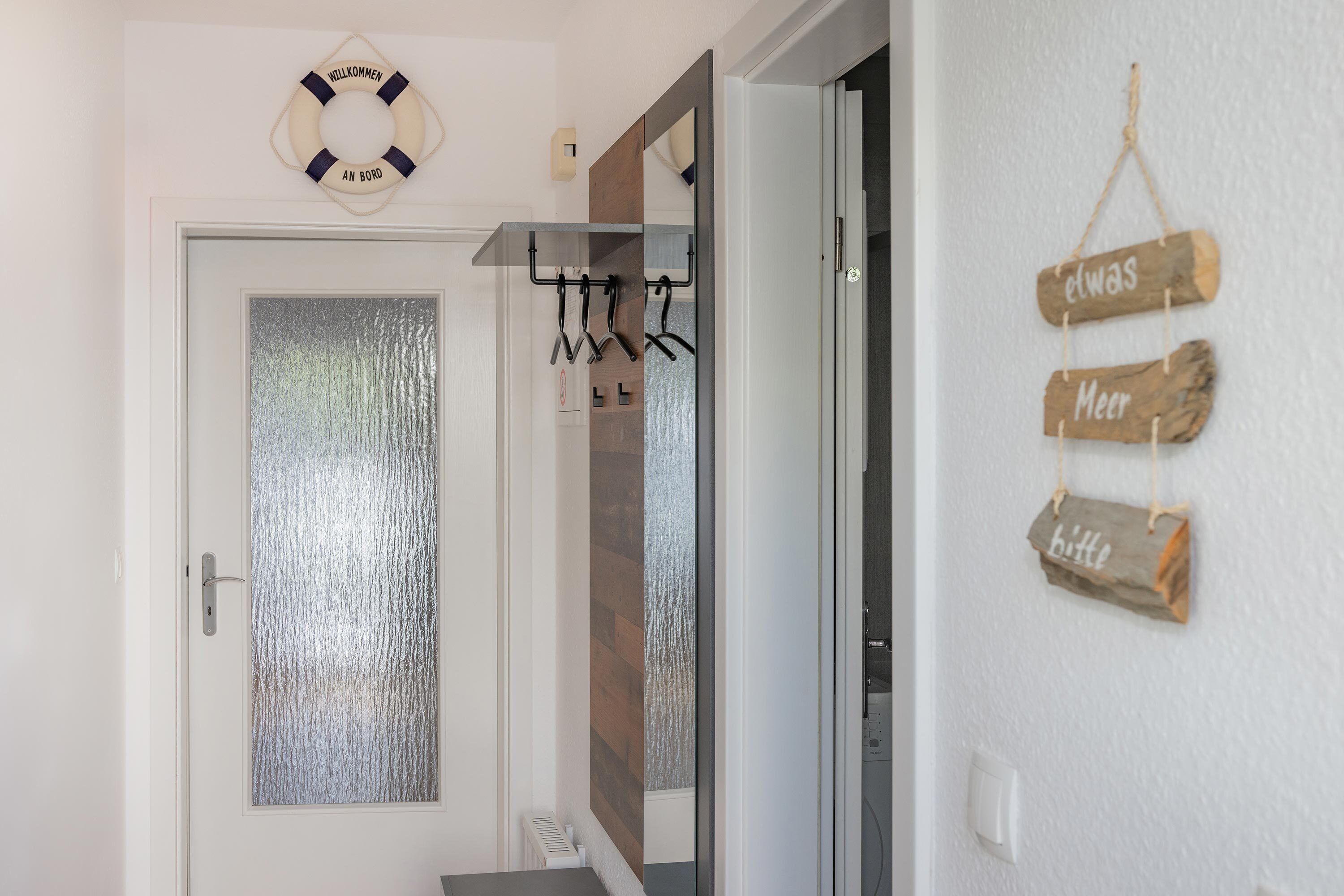 A hallway with a frosted glass door, a life preserver decoration, a coat rack, and a wall with wooden signs.