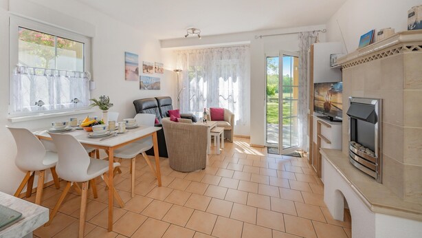 A well-lit, open-plan living space with a dining area, seating, and a fireplace. - Moderne Ferienwohnung mit Gartenblick in Koserow (Koserow)
