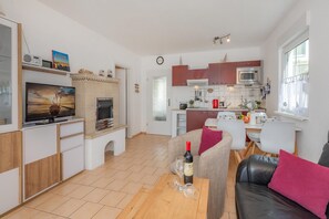 A modern living room with a fireplace, a television, and a dining area with a kitchen in the background. - Moderne Ferienwohnung mit Gartenblick in Koserow (Koserow)