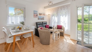 A modern living room with a dining area, featuring a sofa, chairs, a coffee table, and artwork on the walls. - Moderne Ferienwohnung mit Gartenblick in Koserow (Koserow)