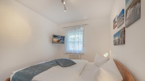 A bedroom with a bed, a window with curtains, and wall-mounted pictures. - Moderne Ferienwohnung mit Gartenblick in Koserow (Koserow)