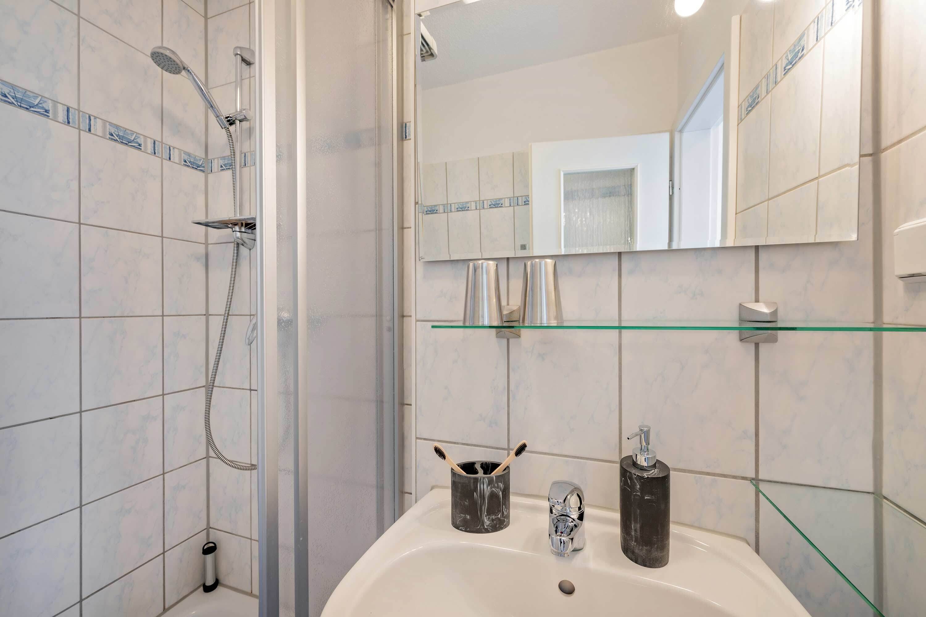 Ein Badezimmer mit Dusche, Waschbecken, Ablage und Spiegel.