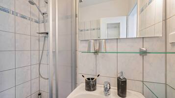 Ein Badezimmer mit Dusche, Waschbecken, Ablage und Spiegel.