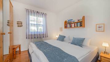 Ein Schlafzimmer mit Bett, Nachttisch, Lampe, Bücherregal, Fenster mit Vorhängen und einem Holzschrank.
