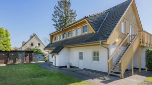 Une maison à deux étages, avec un toit en pente, un escalier en bois et un petit jardin à l’avant.