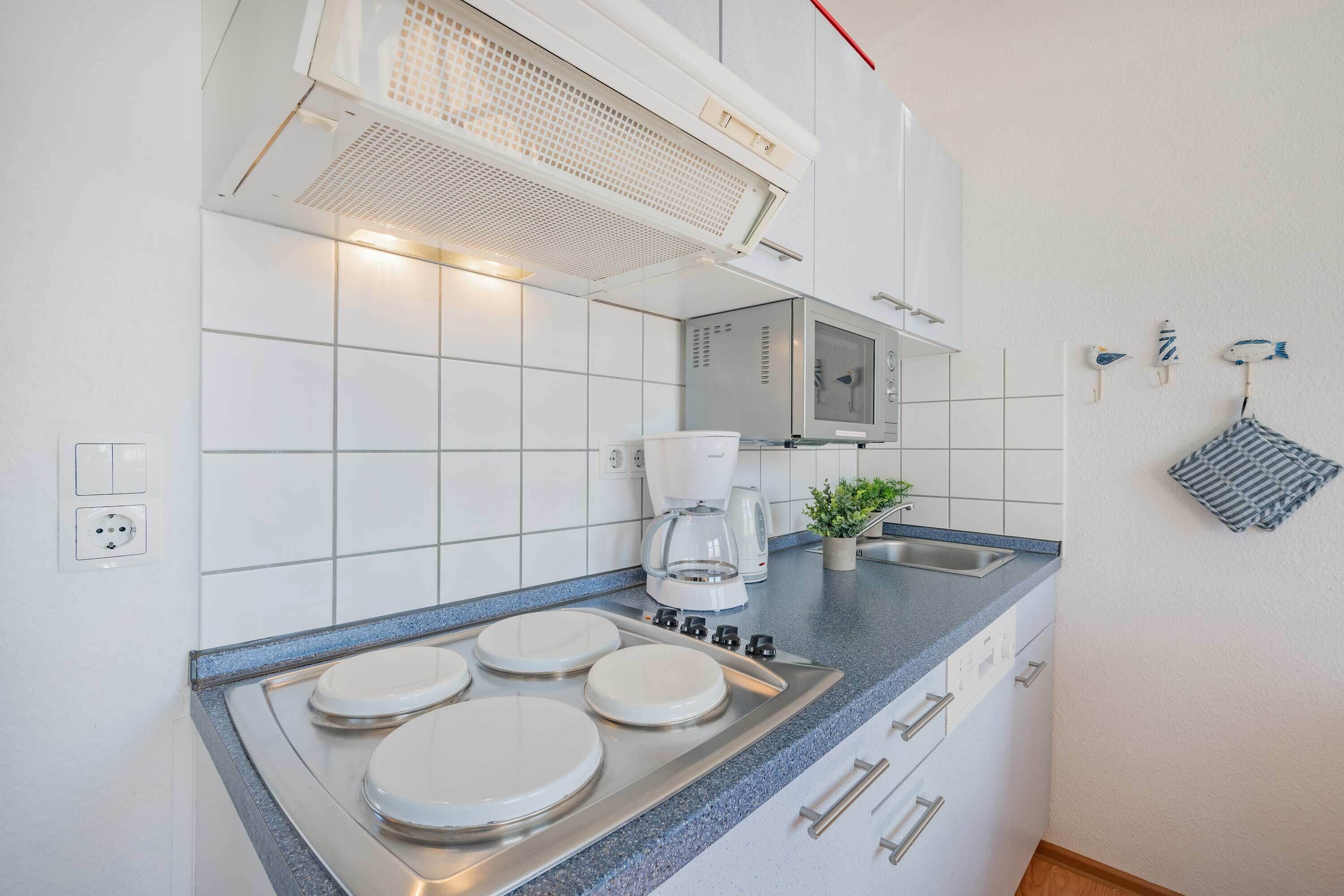 Una cucina moderna con piastrelle bianche, un piano cottura in acciaio inossidabile, una macchina da caffè e un lavandino.