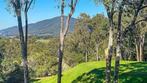 A golf course with a flagstick, surrounded by trees and a hilly landscape.