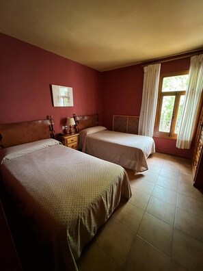 Une chambre avec deux lits, une table de chevet avec une lampe, une fenêtre avec des rideaux et un tableau au mur.
