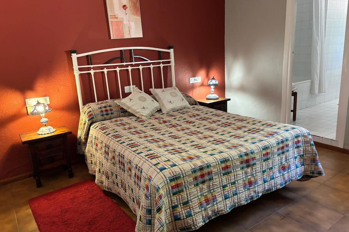 Ein Schlafzimmer mit einem Bett, zwei Nachttischen, einem roten Teppich, einem Bild an der Wand und einer Badezimmertür.