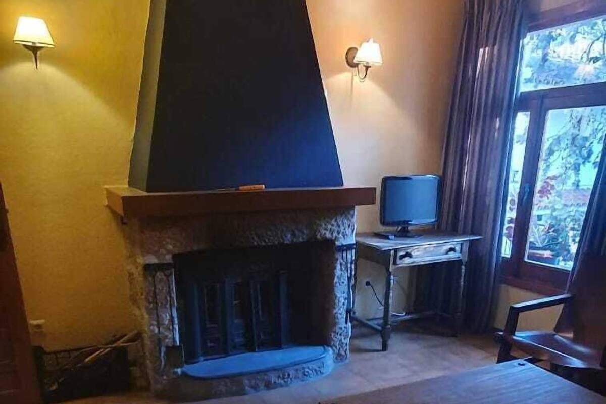 Ein Wohnzimmer mit Kamin, Fernseher auf einem Schrank, einem Sessel und einem Teppich.