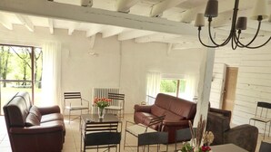 A spacious living room with a dark wooden table, two leather sofas, and a dining table set for four.