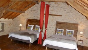 A rustic bedroom with two beds, wooden beams, stone walls, and a sloped ceiling.