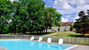 A swimming pool with white lounge chairs and a wooden deck, surrounded by trees and a white picket fence.