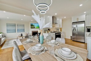 A modern kitchen with white cabinets, a stainless steel refrigerator, and a dining area set with white plates, bowls, and glassware. - 30% OFF / Easy Parking / Mins to SF / Lovely Backyard / Skyline View / Hottub (Daly City)