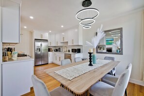 A modern kitchen with white cabinets, stainless steel appliances, and a wooden dining table with a white runner.