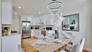 A modern kitchen with white cabinets, stainless steel appliances, and a dining area with a wooden table set for four. - 30% OFF / Easy Parking / Mins to SF / Lovely Backyard / Skyline View / Hottub (Daly City)