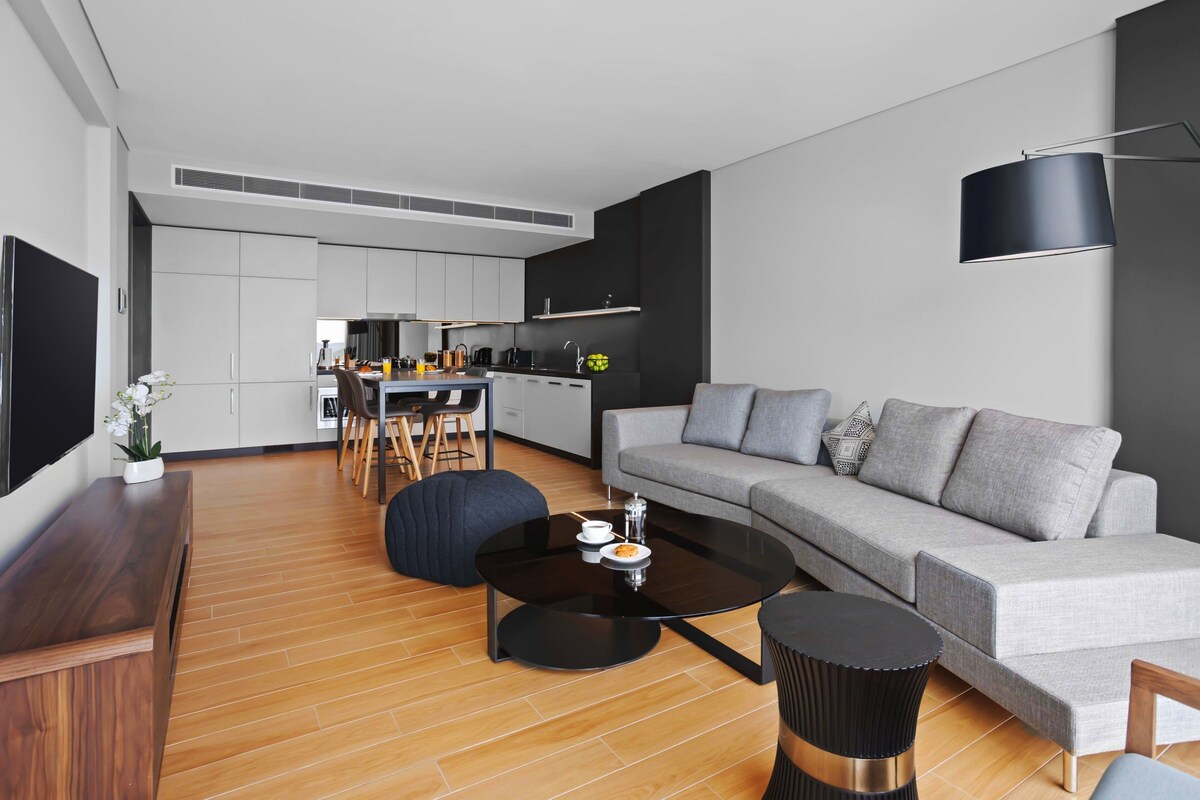 A modern living room with a grey sofa, a black coffee table, and a dining area with a white table and chairs.