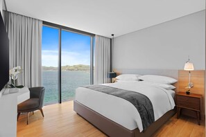 A modern hotel room with a large bed, a desk, and a view of the sea. - Marriott Executive Apartments Port Moresby (Port Moresby)