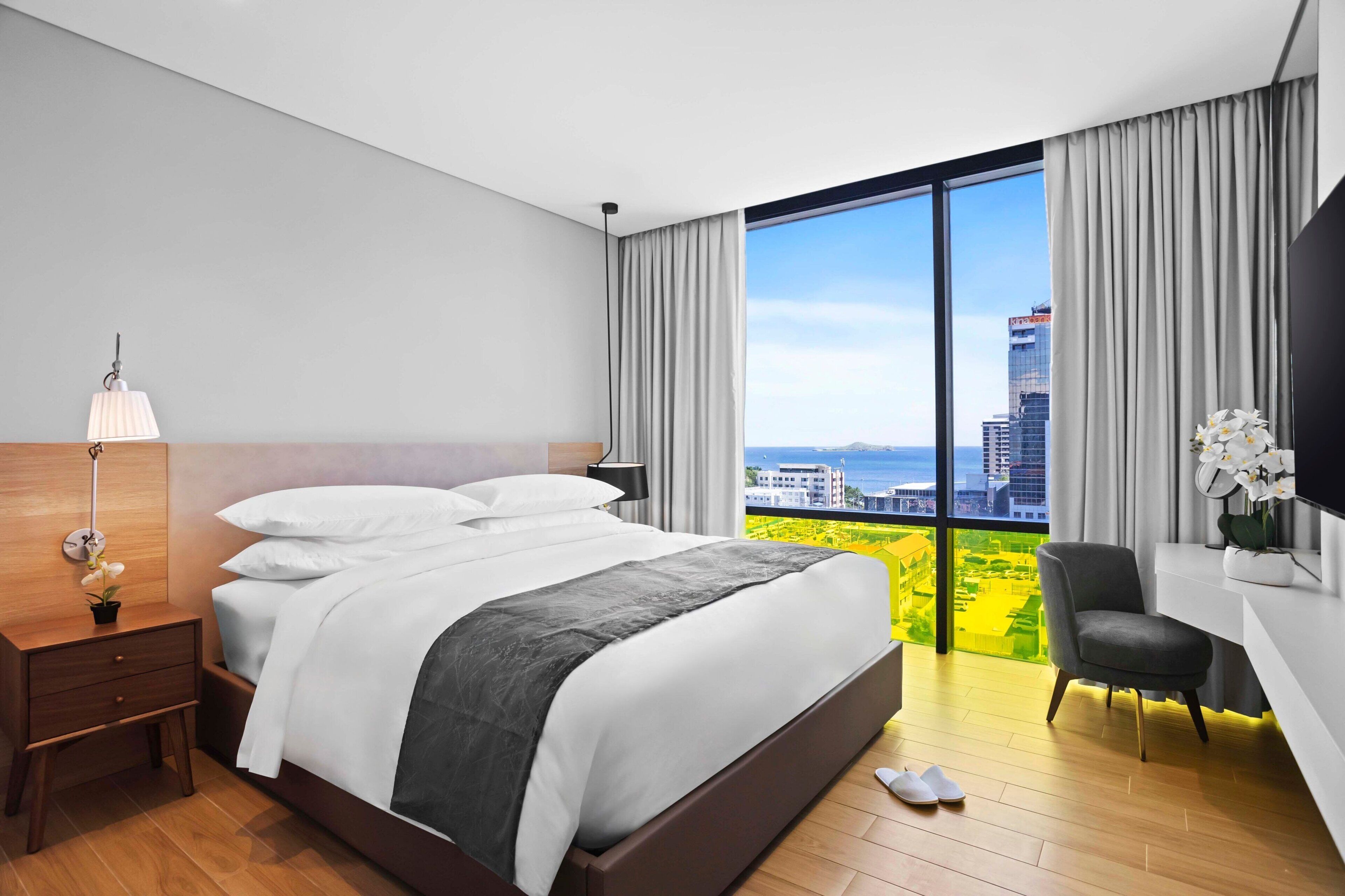 A modern hotel room with a large bed, a desk, a chair, and a TV.