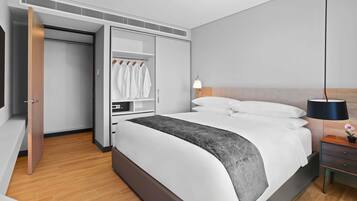 Et moderne hotelværelse med en stor seng, et garderobeskab med tøj, et natbord med en lampe og en lille plante.
