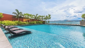 A swimming pool with lounge chairs, surrounded by greenery and a view of the sea. - Marriott Executive Apartments Port Moresby (Port Moresby)