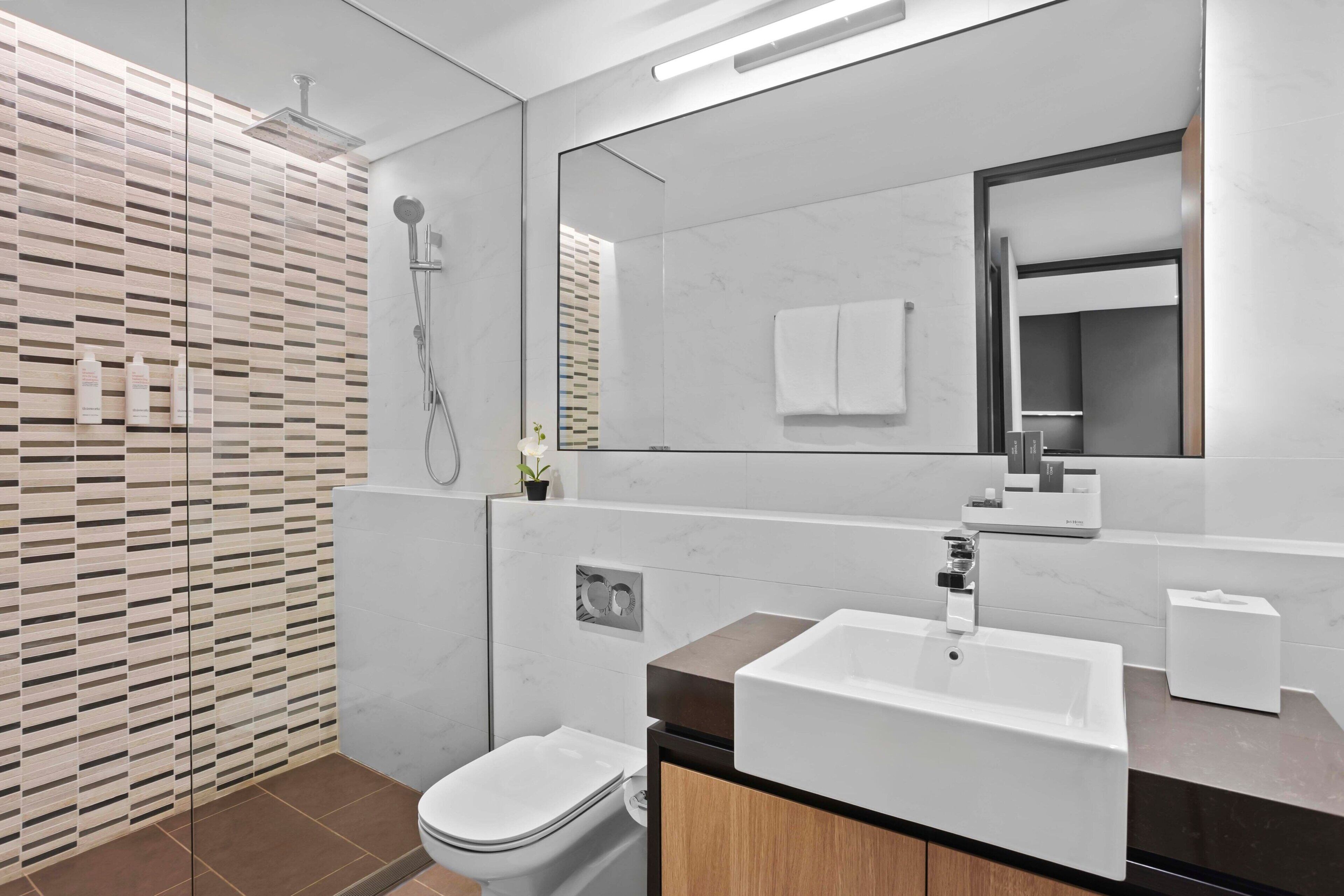Een moderne badkamer met een grote spiegel, een witte wastafel en een douche.