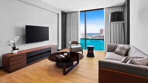 A modern living room with a flat-screen TV, a wooden entertainment unit, a round coffee table, a grey sofa, and a view of the ocean through large windows. - Marriott Executive Apartments Port Moresby (Port Moresby)